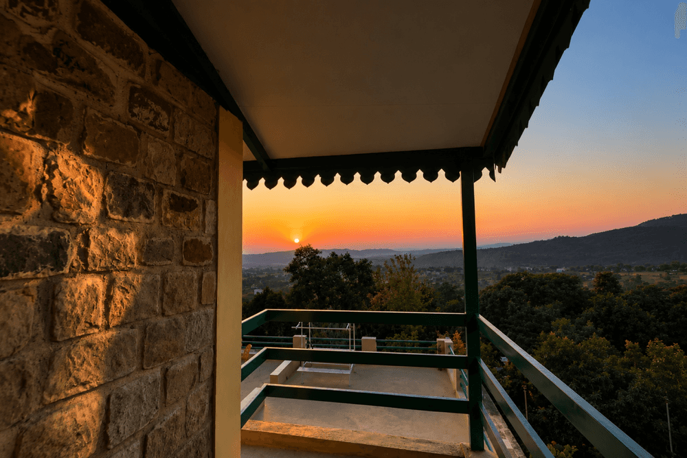 Covered balcony with a view of the sun setting behind the hills