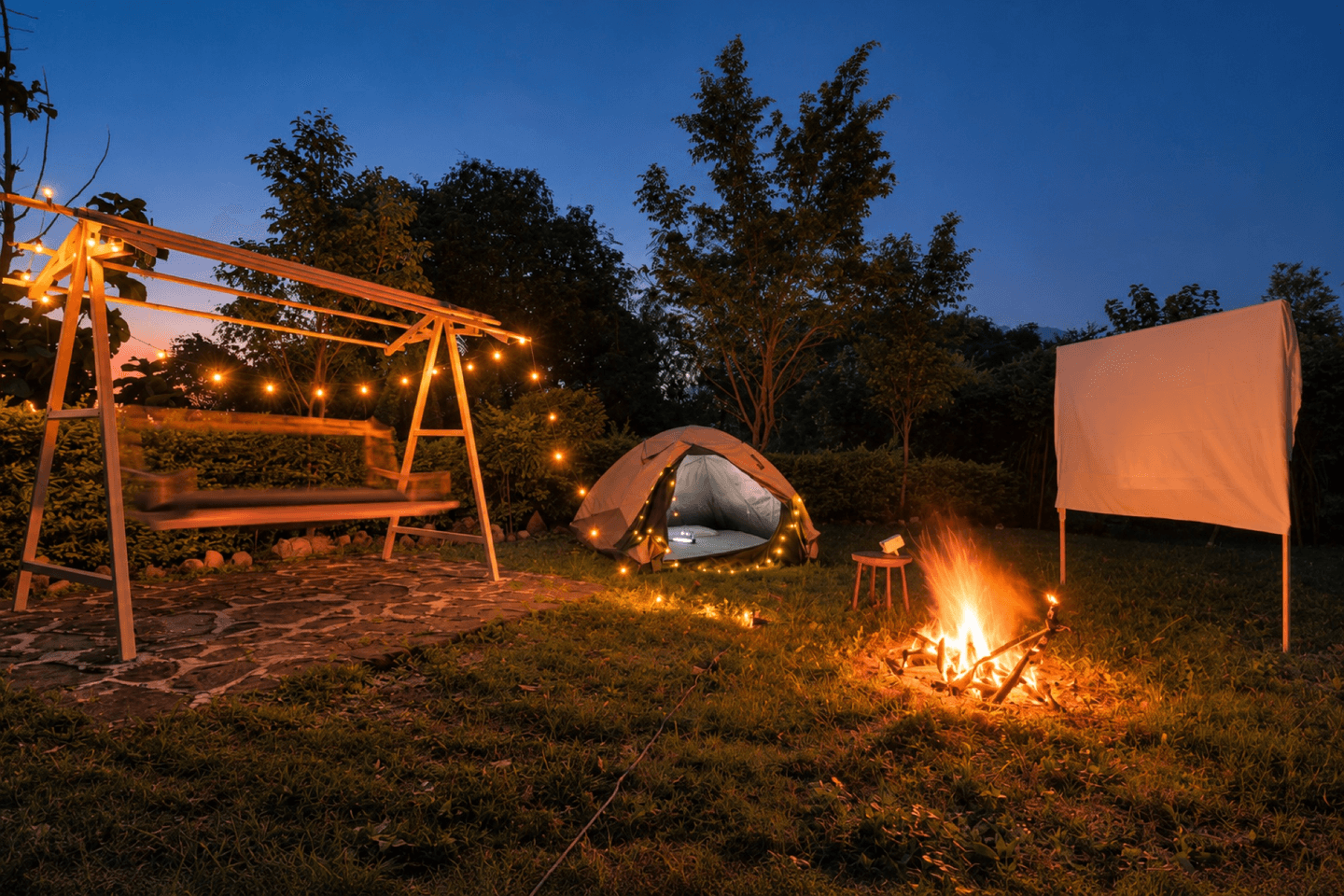 Bonfire, camping tent and fairy-lit swing on the lawn at night